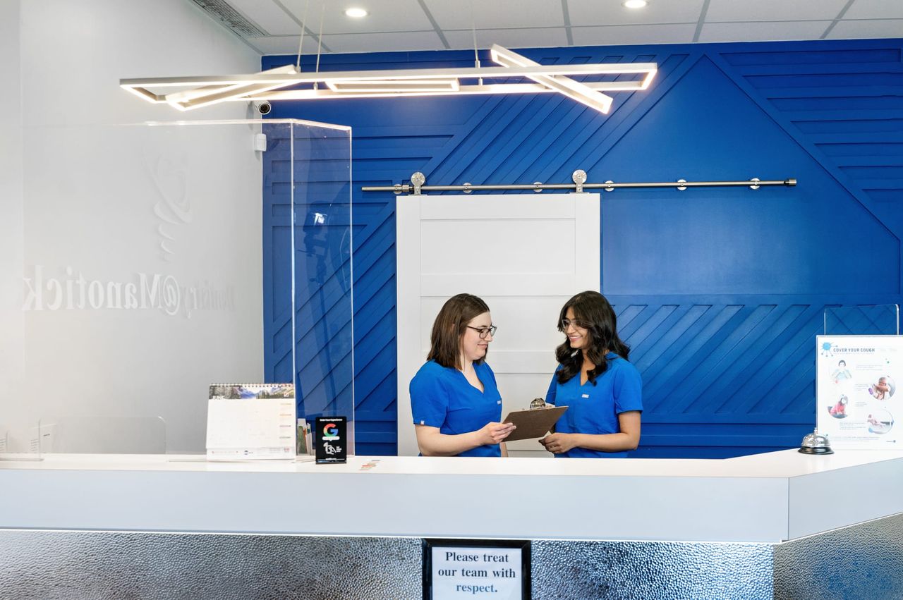 Two team members in blue scrubs at the Dentistry @ Manotick reception desk